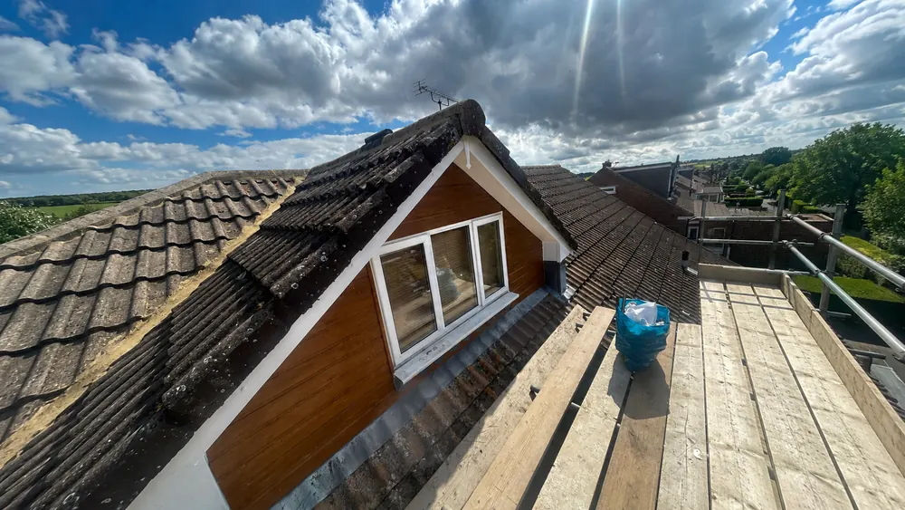 Scaffold platform beside a tiled dormer with a white-framed window and weathered concrete roof tiles