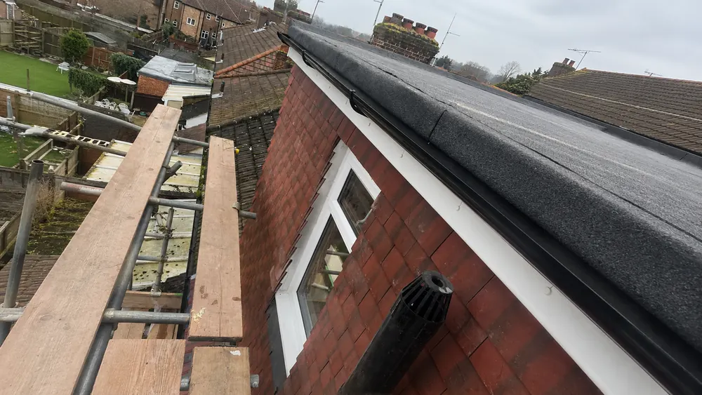 Flat roof on a tile-hung dormer with a white fascia and black guttering, scaffold boards alongside