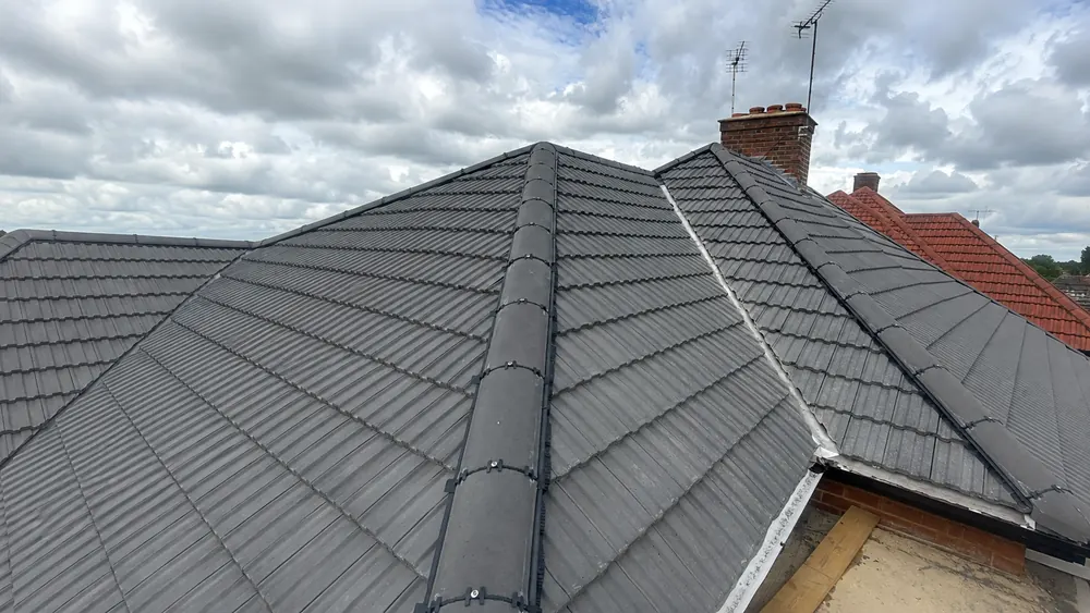 Grey interlocking tiles on a hipped roof with dry-fixed ridge and hip tiles and a brick chimney behind