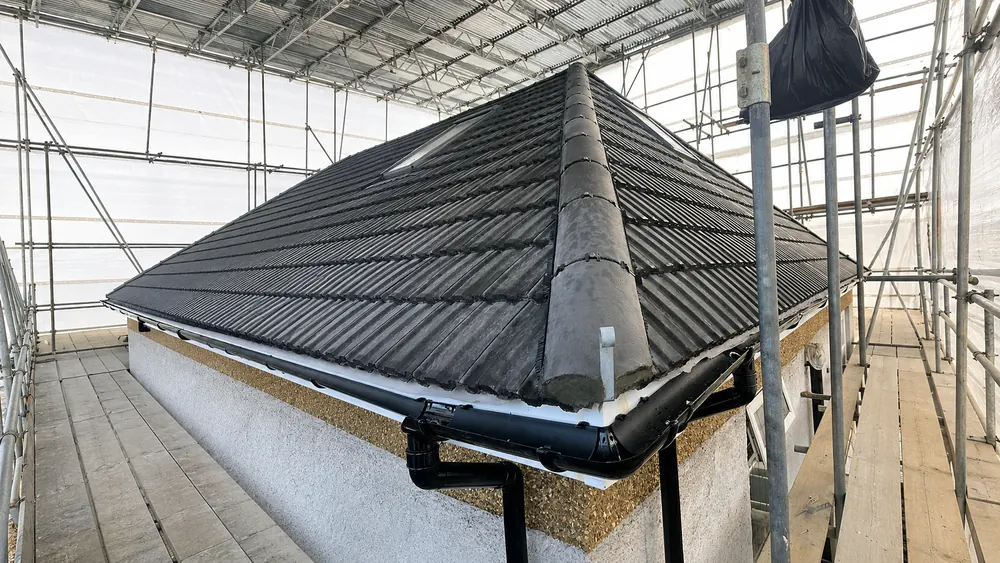 Newly tiled dark hipped roof with black guttering, seen from scaffolding under a temporary cover