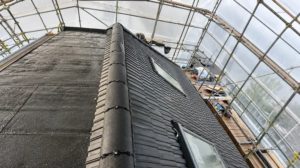 Dark tiled roof with ridge tiles and roof windows inside a sheeted scaffold temporary roof